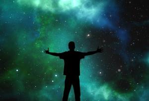 a person with outstretched arms in silhouette against the stars in a night sky