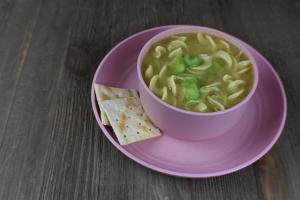 a bowl of chicken soup with crackers on a table