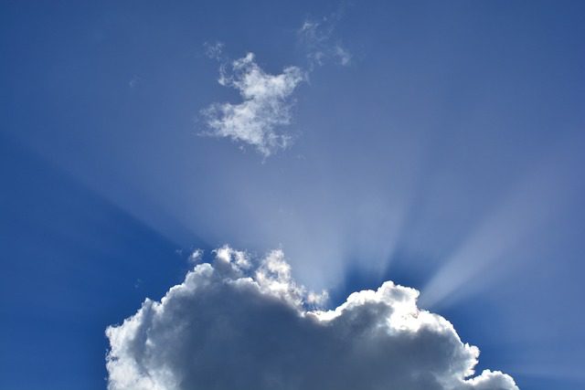 A bright blue sky with clouds, and the sun's rays showing behind the clouds