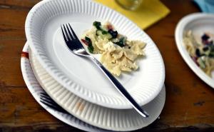 a messy stack of paper plates, with food and a fork on the top one