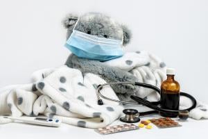 a teddy bear wearing a mask, with a stethoscope and a bottle of cough medicine