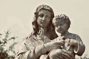 a worn and pitted statue of Mother Mary, holding the baby Jesus, pointing to His Heart
