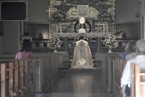 A priest kneels before the Monstrance with the Blessed Sacrament as his congregation looks on