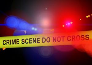 police tape with "crime scene do not cross" on it, in front of the blurry lights of a police car