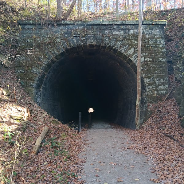 A gray brick railroad tunnel, with a trail running through it.
