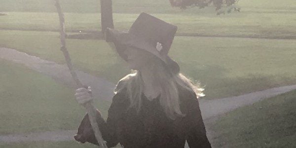 Woman with pointy hat and staff of witchcraft, looks back over the path she's walked.