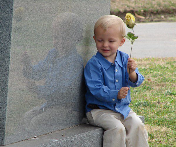 boy holds rose and sits on a gravestone.