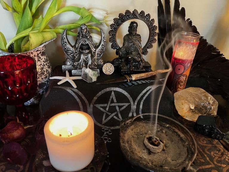 A Witch's Altar with candle, incense burning, chalice, athame, and statues of the Goddess and God