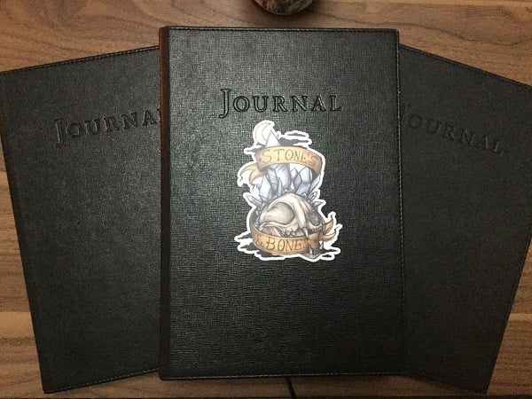 Three of my black books where I record my most important lore. Photo by Coby Michael. Art sicker by Zaheroux.