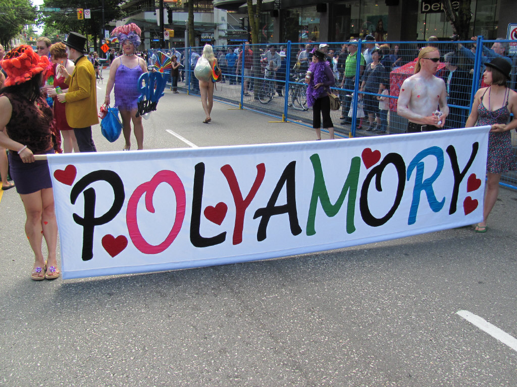 Marchers carry a sign reading "polyamory."