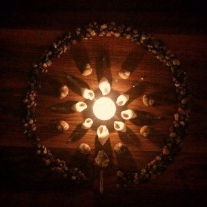 A mandala of stones and shells with a candle in the center.