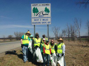 a group of druids holding filled trash bags along the expressway, under the road sign with their name on it.