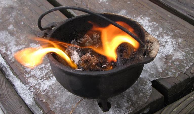 a small cauldron with a fire sitting on a deck with the last bits of ice and snow covering the wood.