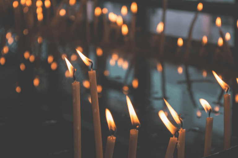 Thin taper candles burning in a slight breeze against a dark background.