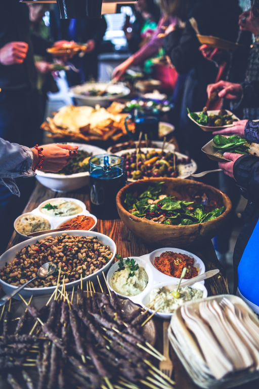 A long buffet style table filled with food where people are reaching in to share and eat. 