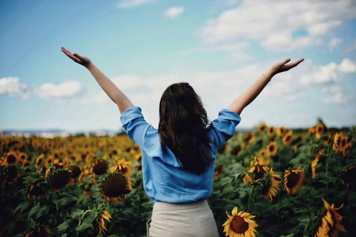 woman raising hands in field of sunflowers