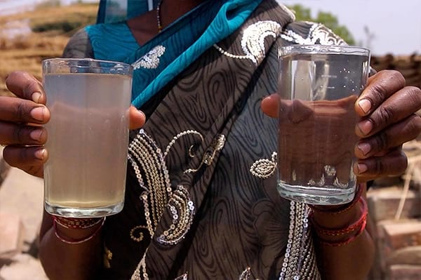 Woman holding glasses of clean and dirty water.