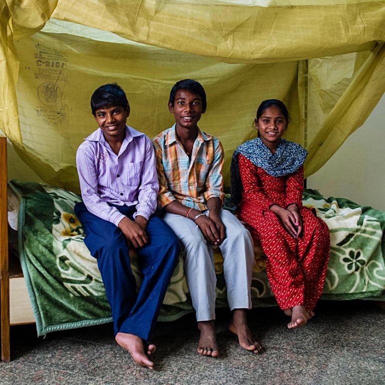 Children sitting on a bed with Mosquito Net covering.