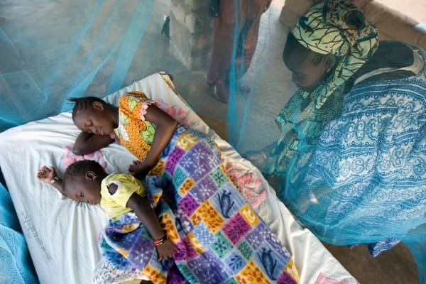 A mother watching her children sleep inside a mosquito net covered bed.