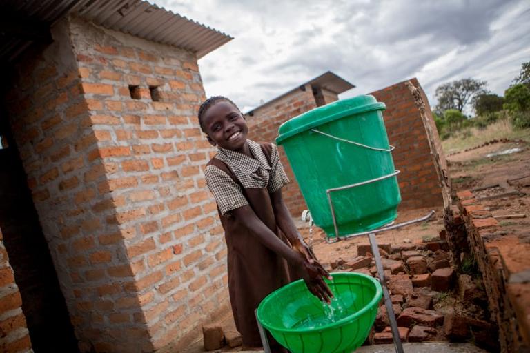 A student washing her hands outside latrines.