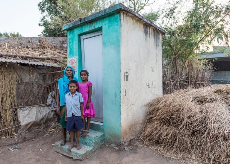 Mother and children outside outdoor toilet