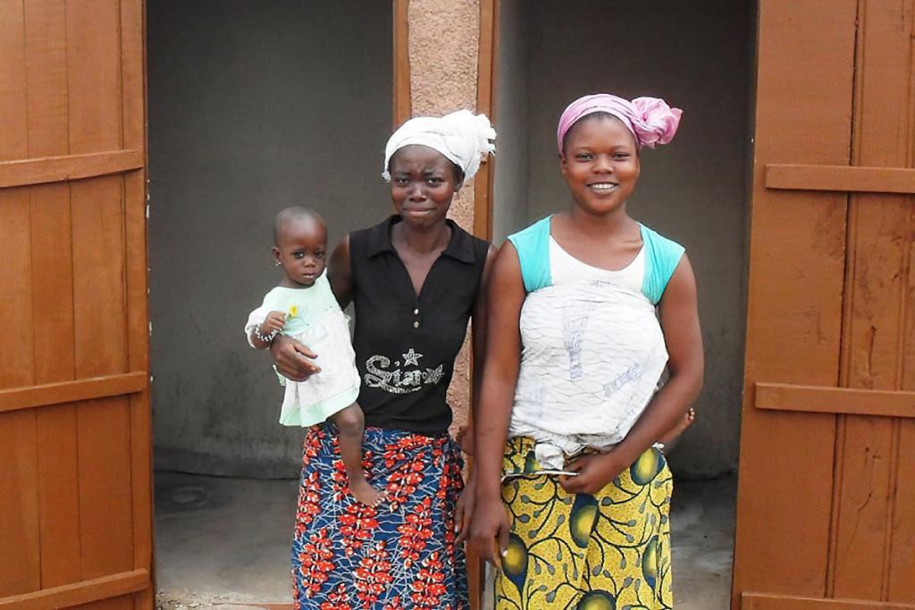 Two women and child outside of outdoor toilet