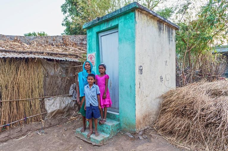 Mother with her son and daughter in front of an outdoor toilet gifted through GFA World donors