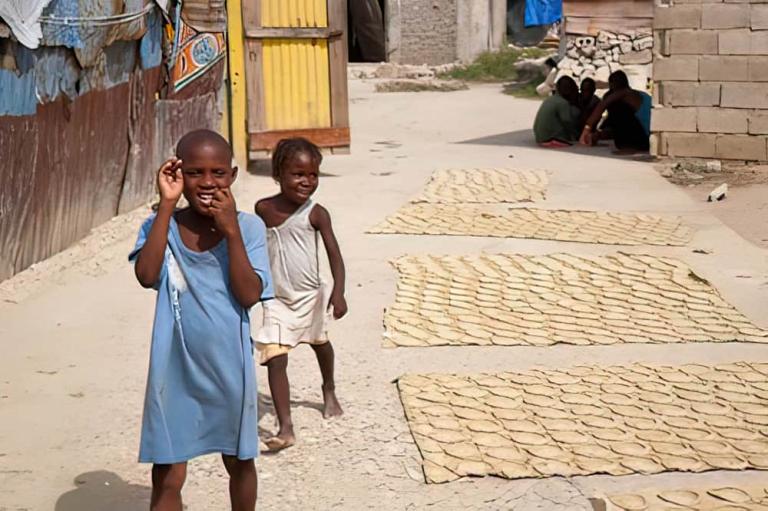 Children in poverty from Haiti walks by mud cakes drying in the sun