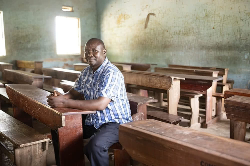 Phanuel Mwami, 48, sits in the classroom at the school he attended as a child
