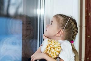 A little girl with a toy sits on the windowsill and draws on the window