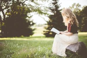 woman sitting on a rock reading scriptures whys and hows of scripture study