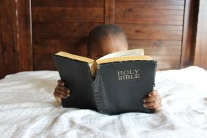 child reading the Holy Bible on the bed