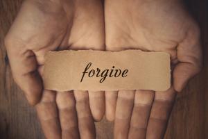Hands holding piece of paper with word Forgive