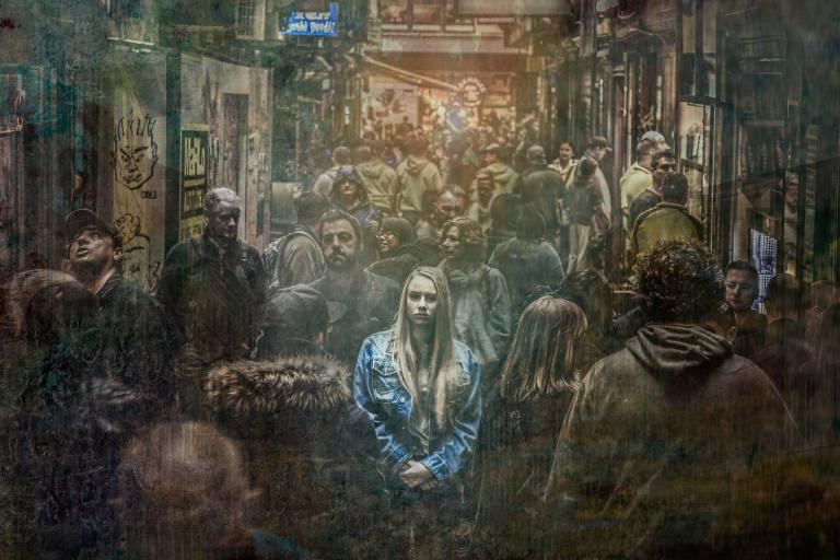 a girl in a blue jacket stands in the middle of a crowded train, but everything else is grungy shades of brown; an image of isolation