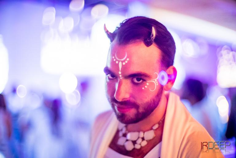 a male witch with small satyr horns, white paint design on his brow, and beautifully layered pink and blue lighting