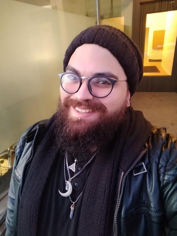 a bearded witch with round glasses and a big smile