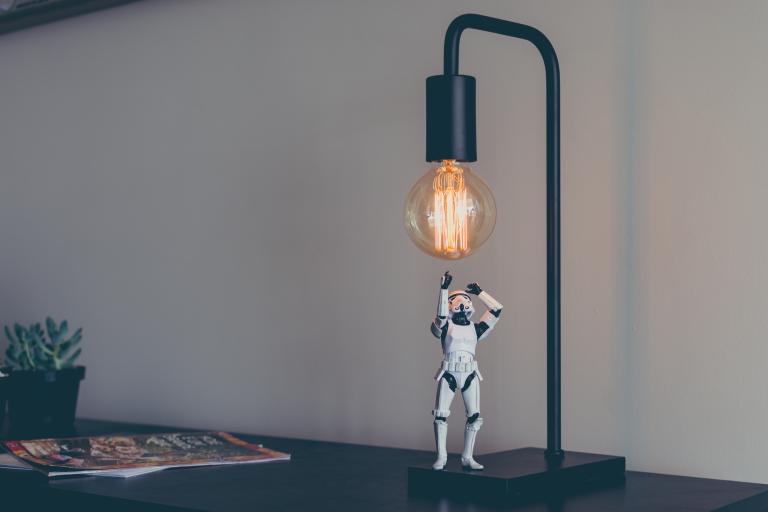 a stormtrooper toy posed to reach for a bare lit lightbulb