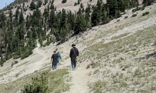 Three figures on a mountainside, following a dusty path.
