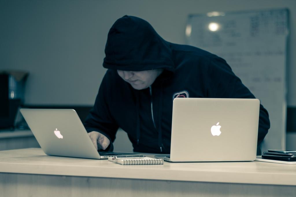 Man in black on two laptops who looks like he might be a hacker