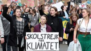 Greta Thunberg, surrounded by young protesters, holds a sign "Skolstrejk for Klimatet."