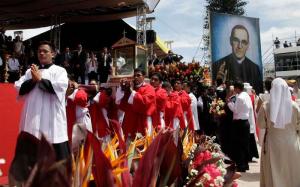 Clerics and a long line of lay people march in procession. Someone is holding a large poster of Oscar Romero.