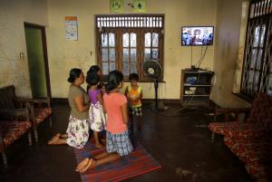 Family members at home kneel before a TV broadcasting Mass.