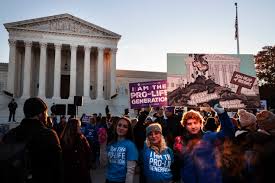 Demonstrators oppose Roe v Wade before the U.S. Supreme Court building, holding signs, e.g., "I am the pro-life generation."