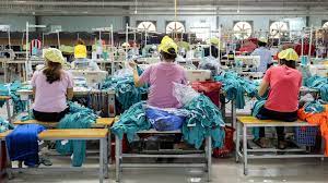 Asian factory workers engaged in sewing machine work. Many desks in the room are empty.