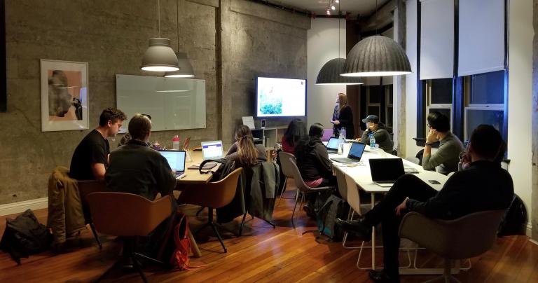 group of adult students sitting at a large table working on computers and discussing
